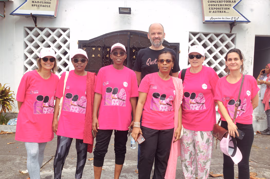 Groupe de personnes posant ensemble, plusieurs portant des t-shirts roses et des casquettes assorties, lors d’un événement solidaire. 