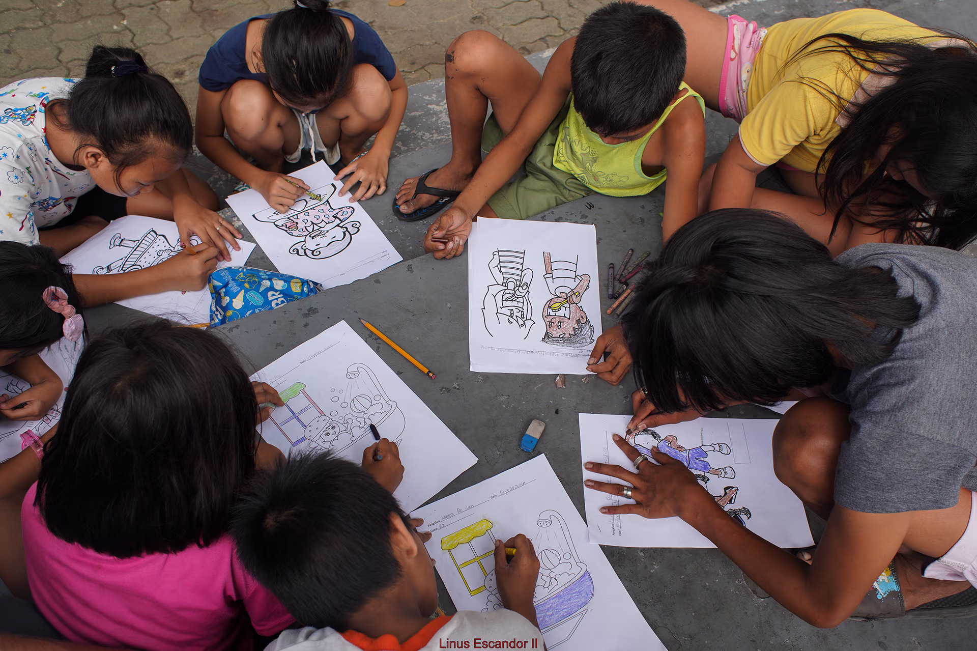 Grupo de niños sentados en el suelo coloreando dibujos en hojas de papel, concentrados en su actividad.