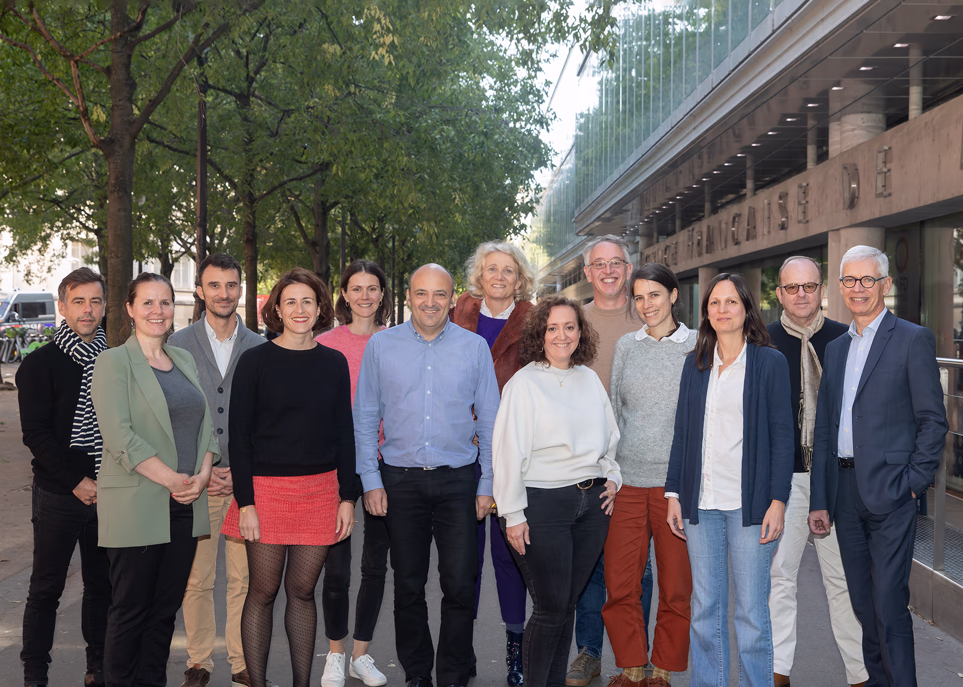 Groupe de personnes posant ensemble à l’extérieur devant un bâtiment moderne, souriant à la caméra.