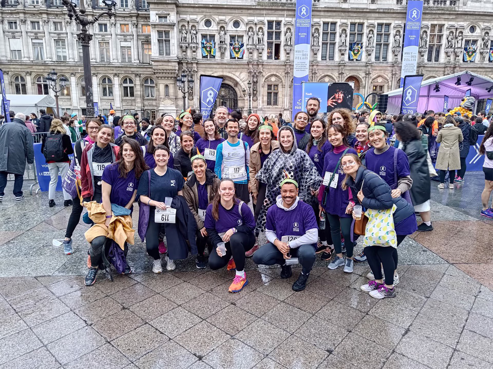 Groupe de participants posant ensemble sur une place devant l’Hôtel de Ville, lors d’un événement sportif ou caritatif.