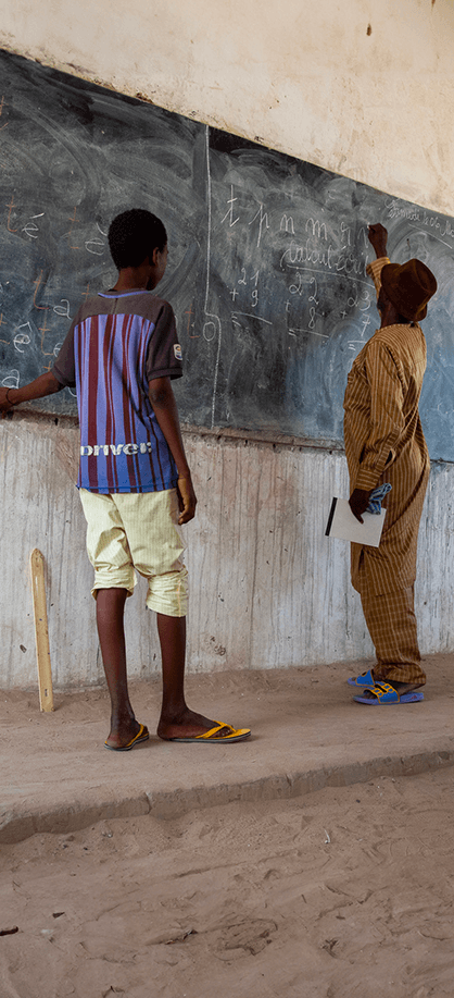 Teacher writing on a blackboard with a pupil beside him in a classroom